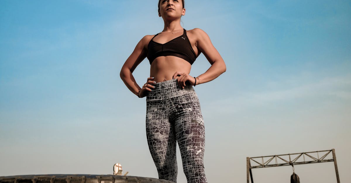 A woman in workout attire standing outdoors against a clear sky, with her hands on her hips, exuding confidence and fitness.