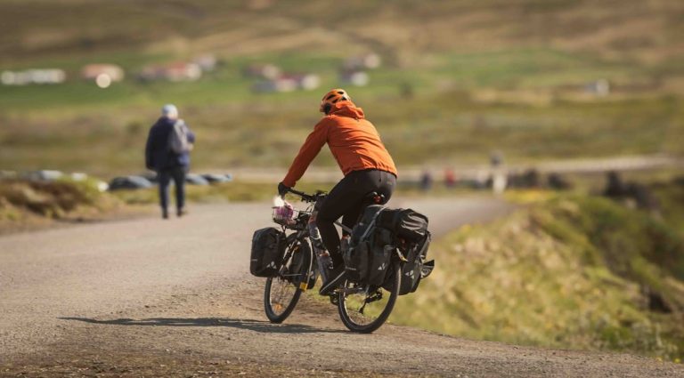 A person biking on a rural road with rolling hills in the background, highlighting sustainable travel through cycling.