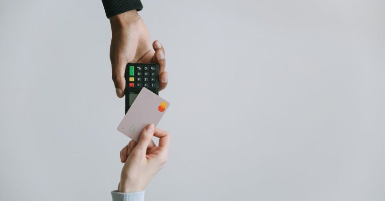 Two hands, one holding a credit card and the other holding a point-of-sale terminal, suggesting digital transactions.