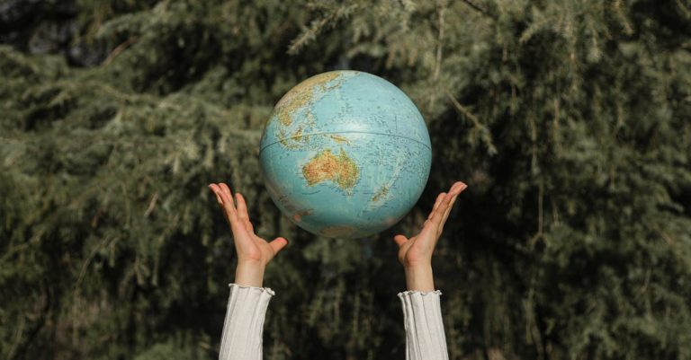 A person holding a globe in their hands with a forest in the background, representing environmental responsibility and sustainability.